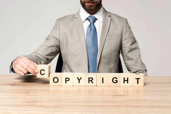 Vista recortada del hombre de negocios sentado en el escritorio cerca de cubos de madera con la palabra copyright aislado en gris — Stock Photo