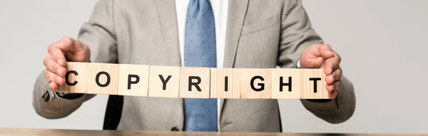 Cropped view of businessman holding wooden cubes with word copyright isolated on grey — Stock Photo