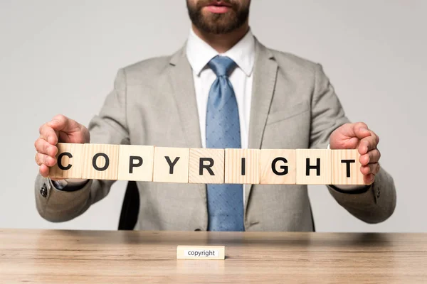 Cropped view of businessman holding wooden cubes with word copyright isolated on grey — Stock Photo