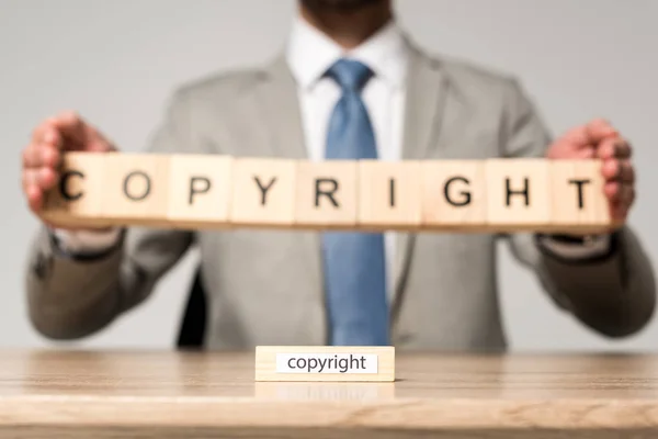 Selective focus of wooden block with word copyright near businessman holding wooden cubes with copyright lettering isolated on grey — Stock Photo