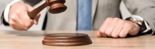 Cropped view of judge holding gavel while sitting at desk isolated on grey, panoramic shot — Stock Photo