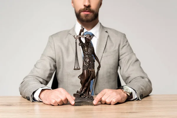 Teilansicht des Anwalts, der die Statue zeigt, während er am Schreibtisch isoliert auf grau sitzt — Stockfoto