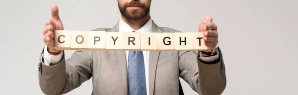 Cropped view of businessman holding wooden cubes with copyright lettering isolated on grey, panoramic shot — Stock Photo