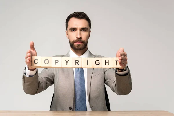 Fiducioso uomo d'affari che tiene cubi di legno con scritte di copyright isolate su grigio — Foto stock