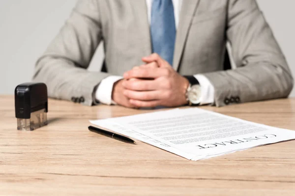 Cropped view of businessman sitting at desk near contract, stamp and pen isolated on grey — Stock Photo