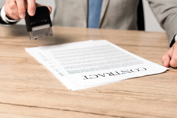 Vista parziale dell'imprenditore che detiene il timbro vicino al contratto isolato su grigio — Foto stock
