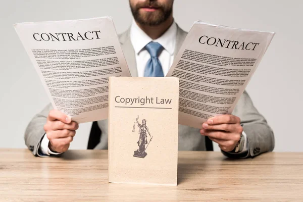 Teilsicht des Rechtsanwalts auf Verträge in der Nähe von Büchern mit urheberrechtlichem Titel isoliert auf grau — Stockfoto