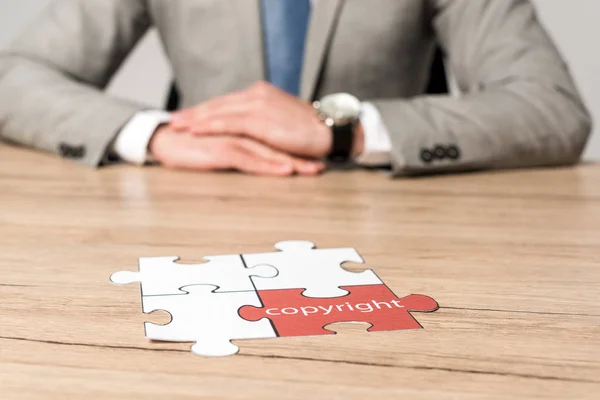 Cropped view of businessman sitting at desk near jigsaw puzzle with word copyright isolated on grey — Stock Photo