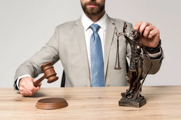 Vista parcial del juez sosteniendo martillo y la estatua de themis aislado en gris - foto de stock