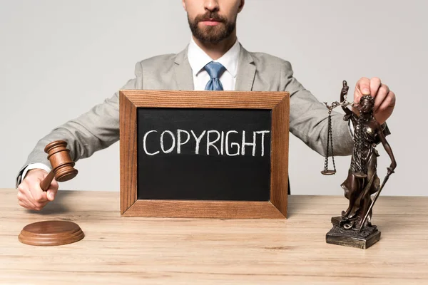 Cropped view of judge holding gavel and themis statue near chalkboard with copyright inscription isolated on grey — Stock Photo