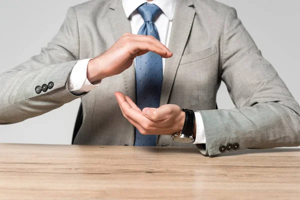 Cropped view of businessman showing protection gesture while sitting at desk isolated on grey — Stock Photo