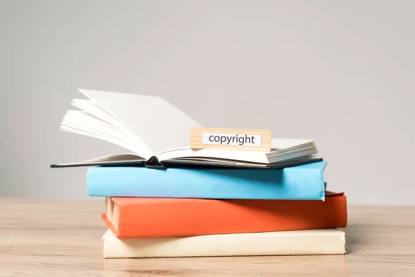 Pila di libri, quaderno aperto e blocco in legno con scritta copyright su scrivania in legno isolata su grigio — Foto stock