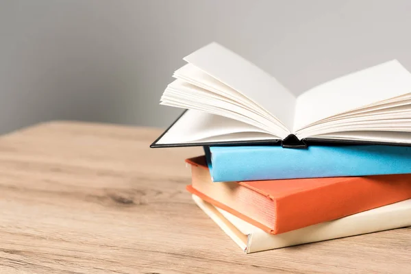 Stack of books and open blank notebook on wooden desk on grey background — Stock Photo