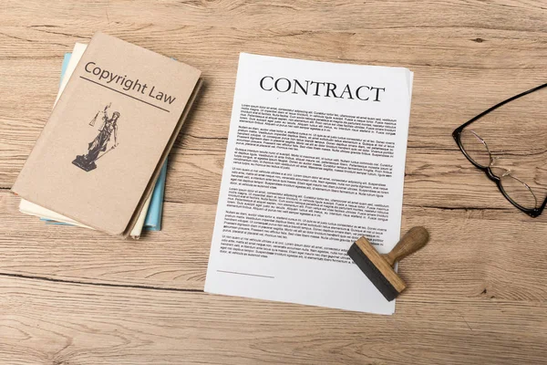 Vista superior del contrato, sello, libros jurídicos y vasos en escritorio de madera - foto de stock