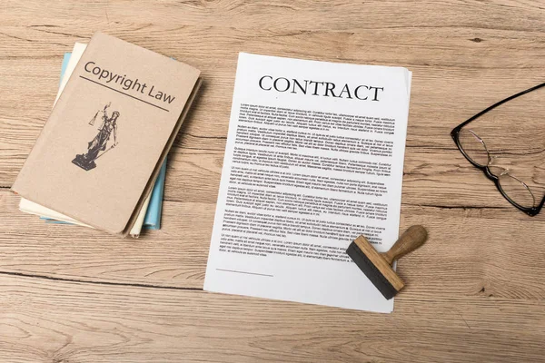 Top view of contract, stamp, juridical books and glasses on wooden desk — Stock Photo