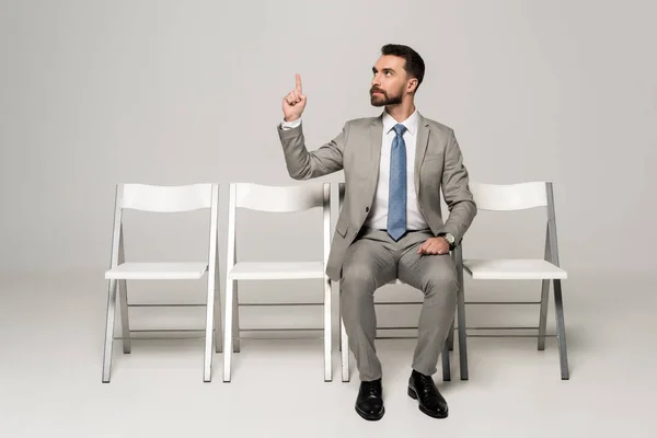 Selbstbewusster Geschäftsmann sitzt auf Stuhl und zeigt Ideengeste auf grauem Hintergrund — Stockfoto
