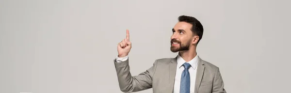 Панорамний знімок усміхненого бізнесмена, що показує жест ідеї ізольований на сірому — стокове фото