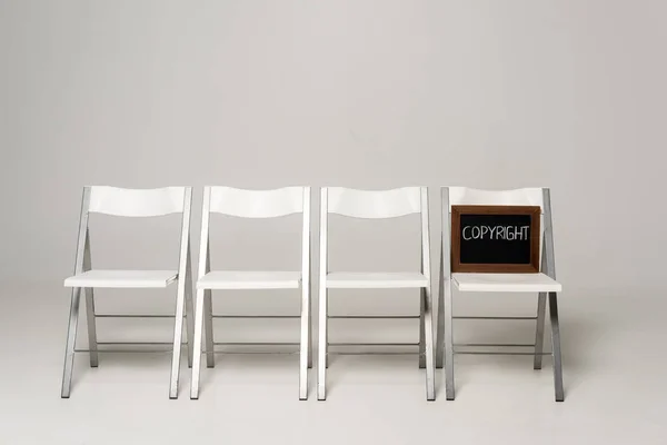 Linha de cadeiras e quadro-negro com inscrição de direitos de autor sobre fundo cinzento — Fotografia de Stock