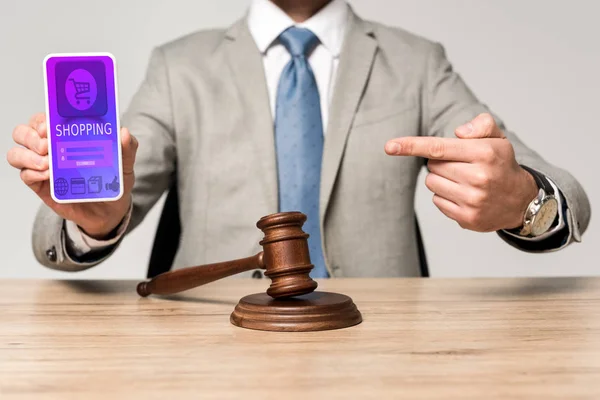Cropped view of lawyer pointing with finger at smartphone with shopping app, and gavel on desk — Stock Photo