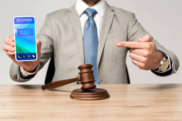 Vista ritagliata dell'avvocato che punta il dito contro lo smartphone con l'app di prenotazione e giudice Gavel sulla scrivania — Foto stock