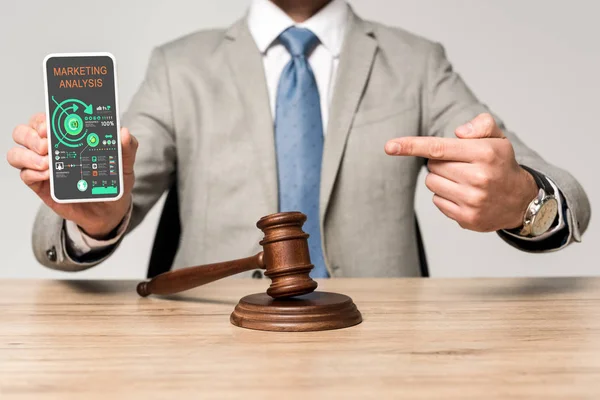 Cropped view of lawyer pointing with finger at smartphone with marketing analysis app, and judge gavel on desk — Stock Photo