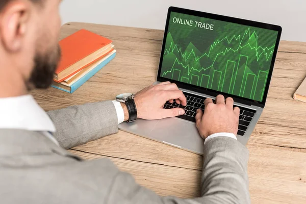 Cropped view of businessman using laptop with online trade website on screen isolated on grey — Stock Photo