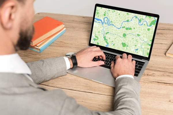 Vista recortada del hombre de negocios utilizando el ordenador portátil con mapa en la pantalla aislada en gris - foto de stock