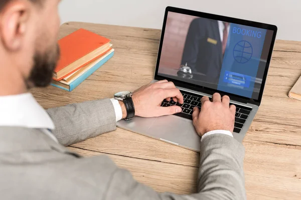 Vista parcial del hombre de negocios utilizando el ordenador portátil con el sitio web de reserva en la pantalla aislada en gris - foto de stock