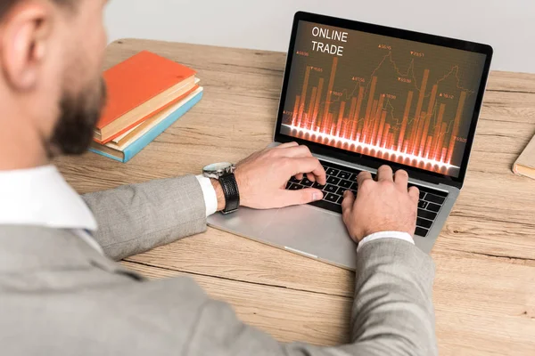 Partial view of businessman using laptop with online trade website on screen isolated on grey — Stock Photo