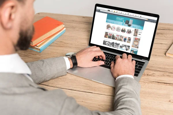 KYIV, UCRAINA - 25 NOVEMBRE 2019: vista ritagliata di uomo d'affari che utilizza laptop con sito web Amazon sullo schermo isolato su grigio — Foto stock