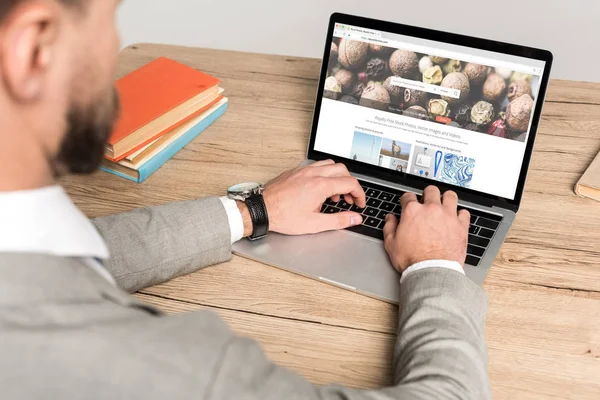 KYIV, UKRAINE - NOVEMBER 25, 2019: cropped view of businessman using laptop with Depositphotos website on screen isolated on grey — Stock Photo