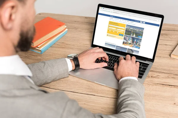 KYIV, UKRAINE - NOVEMBER 25, 2019: cropped view of businessman using laptop with Booking website on screen isolated on grey — Stock Photo