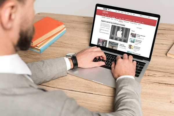 KYIV, UCRANIA - 25 de noviembre de 2019: vista recortada del hombre de negocios que utiliza el ordenador portátil con el sitio web de noticias de la BBC en la pantalla aislada en gris - foto de stock