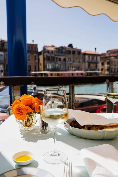 Mise au point sélective du verre à vin, du pain et des fleurs sur la table et des bâtiments anciens sur fond — Photo de stock