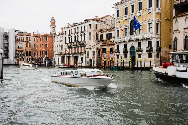 Barcos a motor flotando en el canal cerca de edificios antiguos en Venecia, Italia - foto de stock