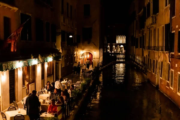 VENICE, ITÁLIA - SETEMBRO 24, 2019: turistas sentados perto de café ao ar livre com vista para o canal à noite em Veneza, Itália — Fotografia de Stock