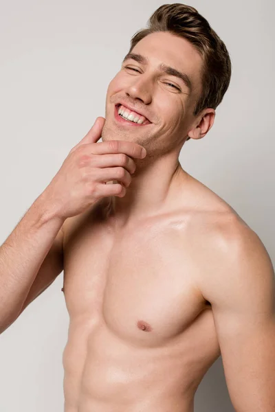 Homme sexy souriant avec torse musculaire toucher menton isolé sur gris — Photo de stock