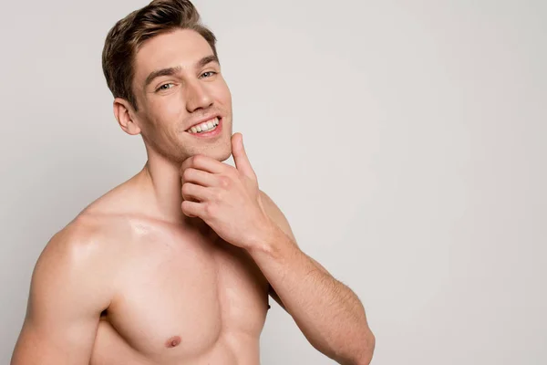 Smiling sexy man with muscular torso touching chin isolated on grey — Stock Photo