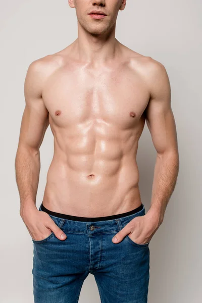 Vista recortada de hombre sexy con torso muscular posando con las manos en bolsillos aislados en gris - foto de stock
