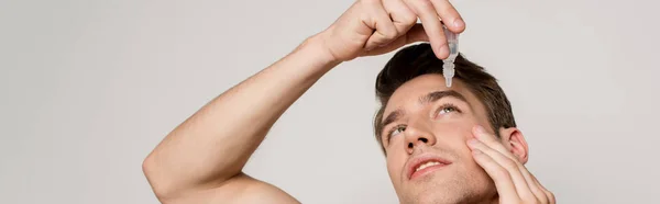 Sexy man using eye drops isolated on grey, panoramic shot — Stock Photo