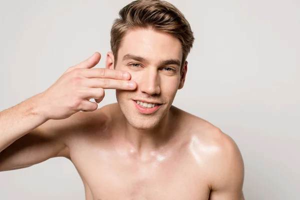 Усміхнений сексуальний чоловік з голим торсом торкається чистого обличчя ізольовано на сірому — стокове фото