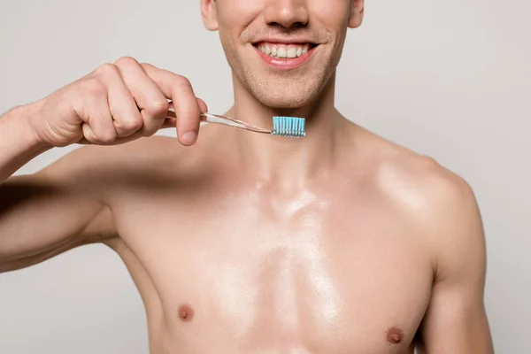 Abgeschnittene Ansicht eines lächelnden sexy Mannes mit nacktem Oberkörper, der eine Zahnbürste isoliert auf grau hält — Stockfoto