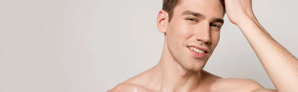 Smiling sexy man with muscular torso touching hair isolated on grey, panoramic shot — Stock Photo