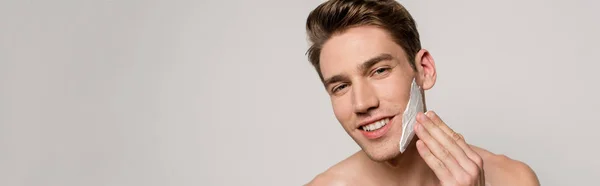 Smiling sexy man with muscular torso applying shaving foam isolated on grey, panoramic shot — Stock Photo