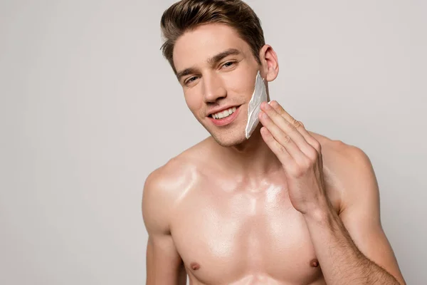 Sorrindo homem sexy com torso muscular aplicando espuma de barbear isolado em cinza — Fotografia de Stock