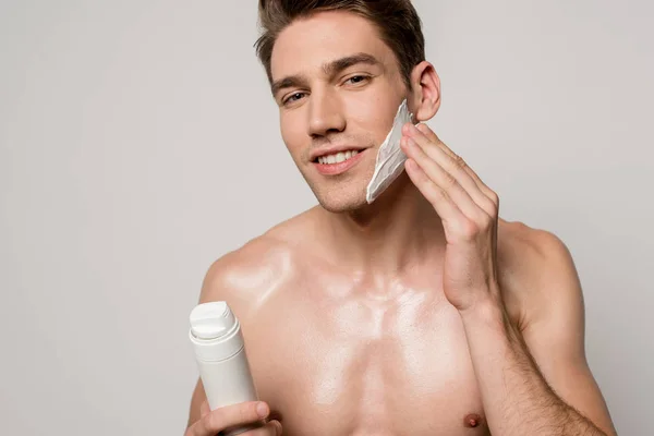 Smiling sexy man with muscular torso applying shaving foam isolated on grey — Stock Photo