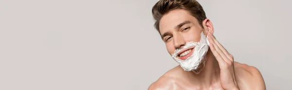 Sorrindo homem sexy com torso muscular aplicando espuma de barbear isolado em cinza, tiro panorâmico — Fotografia de Stock