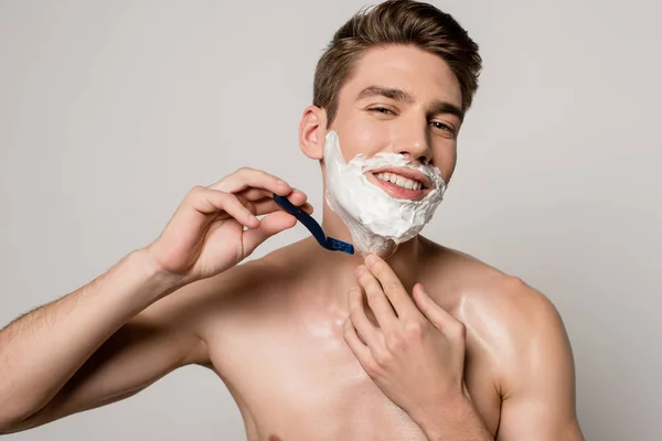 Smiling sexy man with muscular torso shaving isolated on grey — Stock Photo