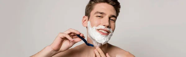 Smiling sexy man with muscular torso shaving isolated on grey, panoramic shot — Stock Photo