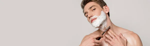 Сексуальный мужчина с мышечным туловищем бритья с прямой бритвой изолированы на сером, панорамный снимок — стоковое фото
